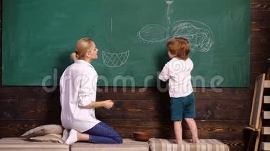 妈妈和她的儿子在学校用粉笔在绿色黑板上<strong>画画</strong>，后视。 女人和<strong>男孩画画</strong>。 回到学校